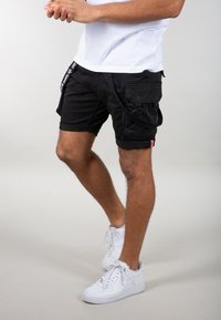 Mustat cargo-shorts useilla taskuilla, joissa on säädettävä naru ja logotagi. Yhdistetty valkoisiin lenkkareihin.