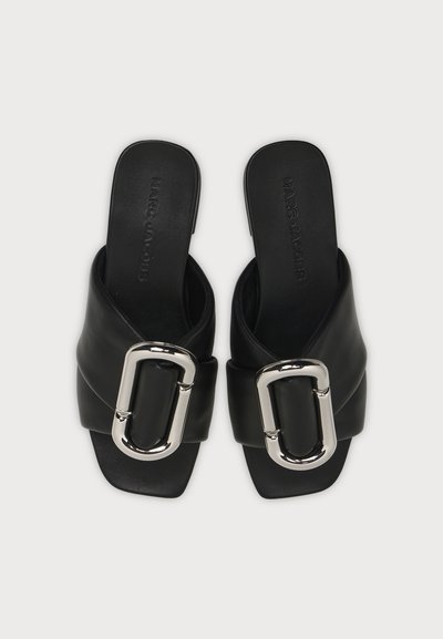Paire de sandales noires à enfiler avec des larges brides et de grandes boucles rectangulaires argentées sur le dessus, avec la marque Marc Jacobs à l'intérieur.