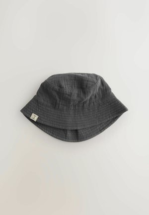 Siva bombažna klobučka z širokim, navzdol nagnjenim robom. Ima teksturirano tkanino in majhno etiketo na strani.