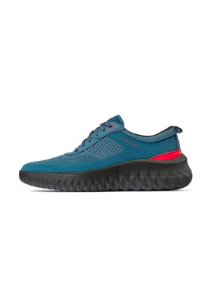 Blaue Mesh-Sneaker mit strukturiertem Obermaterial, ausgestattet mit schwarzen, auffälligen Sohlen und roten Akzenten. Die Schnürsenkel sind gebunden und zeigen ein traditionelles Schuhdesign.