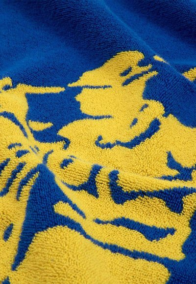 Κοντινή λήψη υφάσματος με υφή, με κίτρινα και μπλε αφηρημένα σχέδια και ανάγλυφες λεπτομέρειες σε μια μαλακή επιφάνεια.