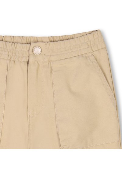 Pantalon en coton beige avec une taille élastique, des poches avant et un bouton visible avec un détail de logo gravé. Texture de tissu lisse et durable.