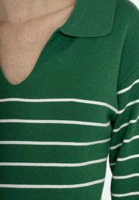 Haut à rayures vertes avec des rayures horizontales blanches, présentant un décolleté en V et un col. Le tissu semble côtelé et ajusté.