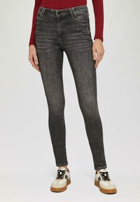 Zwarte denim jeans met een slim fit, voorzien van voorzakken en een vervaagde textuur. Gecombineerd met beige en zwarte sneakers.