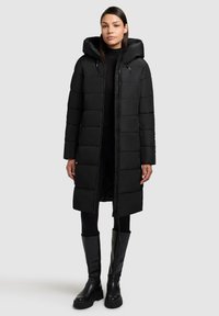 Zwarte gewatteerde lange jas met capuchon, ritssluiting, twee zijzakken en een textuurstofafwerking. Draag het over zwarte leggings en laarzen.