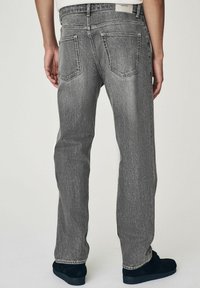 Graue Denim-Jeans mit lockerer Passform, fünf Taschen, geradem Bein und einer leicht abgenutzten Textur. Sichtbare schwarze Schuhe.