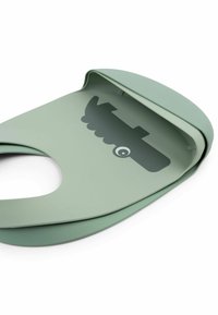 Silikonevoks i afdæmpet grøn med rundede kanter og en lomme. Har et tegneserie-krokodillemotiv i en mørkere grøn nuance. Fleksibelt materiale.