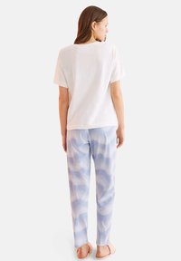 T-shirt bianco in cotone con maniche corte abbinato a pantaloni da pigiama blu con effetto tie-dye. Il tessuto appare morbido con una vestibilità rilassata.