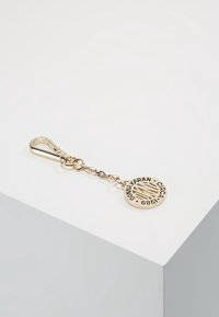 Porte-clés ton or avec un pendentif rond gravé "Donna Karan Circa 1989", attaché à une chaîne et un mousqueton.