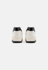 Pair of white and black sneakers with thick soles shown from the back on a plain white background.