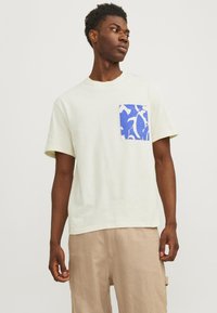 Lys gul kortærmet t-shirt med en blå og hvid mønstret lomme på venstre side. Blødt bomuldsmateriale, afslappet pasform, rund hals.