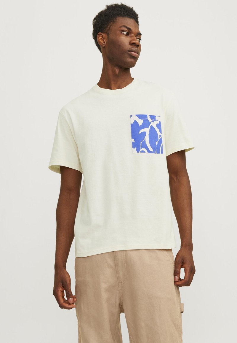 Lys gul kortærmet t-shirt med en blå og hvid mønstret lomme på venstre side. Blødt bomuldsmateriale, afslappet pasform, rund hals.