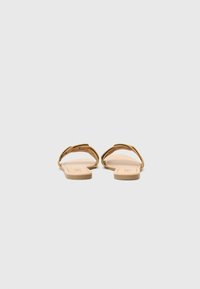Sandales plates beiges avec deux brides croisées à la texture lisse et une semelle en caoutchouc, vues de l'arrière. Design minimaliste.