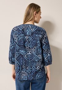 Laivansinisessä paidassa on geometrinen kuvio eri sinisen sävyissä, kolmivartiset hihat ja rento istuvuus.