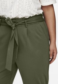 Gröna byxor med bälte som har en jämn textur, sidofickor och en knytning i midjan. Designen har en ren, skräddarsydd passform.