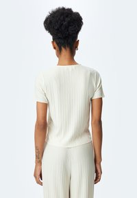 Top de color crema pálido de manga corta con canalé vertical y un dobladillo ligeramente curvado, acompañado de pantalones a juego con canalé. Textura suave y diseño casual.