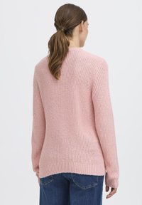 Maglione lavorato a maglia rosa chiaro con finitura testurizzata, maniche lunghe e orlo posteriore leggermente più lungo, abbinato a jeans di denim.
