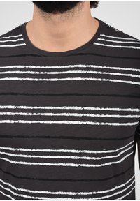 Svart t-skjorte med horisontale hvite og svarte striper, rund hals og myk tekstur. Stripene har et litt slitt utseende.