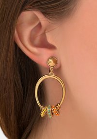 Des boucles d'oreilles en métal doré présentant un design de créole circulaire orné de quatre anneaux colorés en orange, jaune et turquoise.