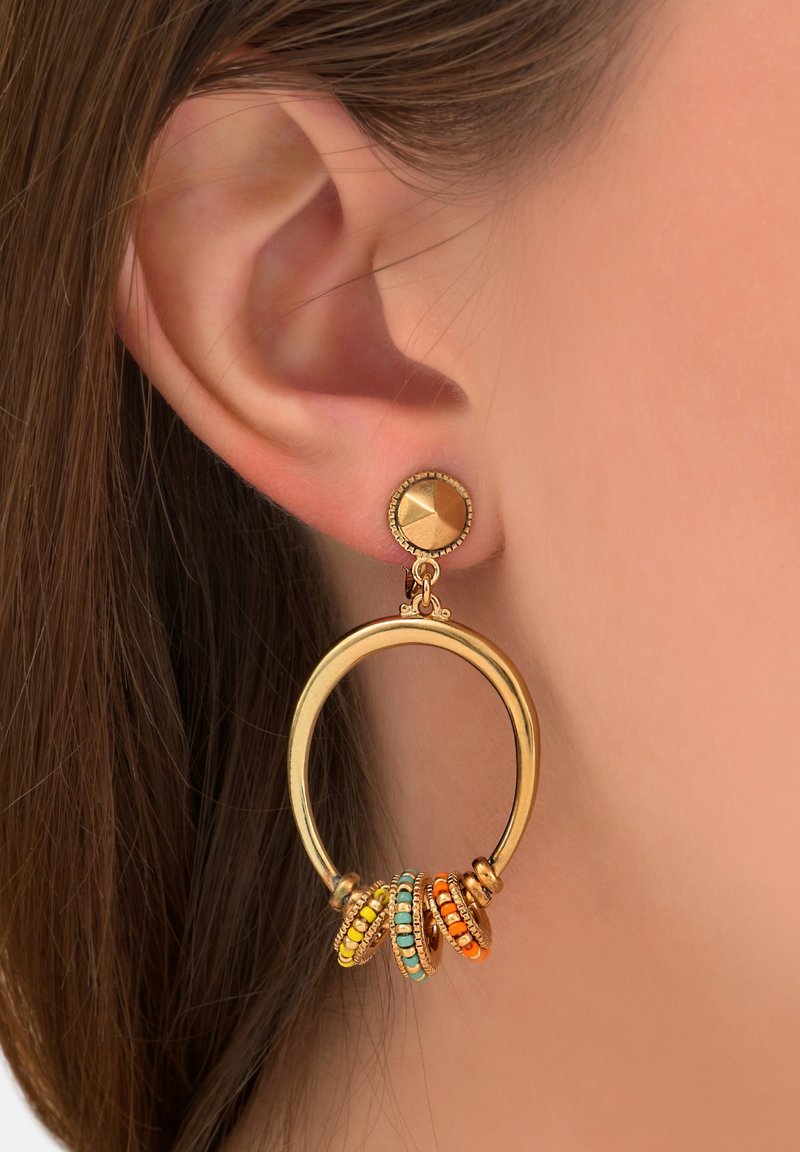 Des boucles d'oreilles en métal doré présentant un design de créole circulaire orné de quatre anneaux colorés en orange, jaune et turquoise.