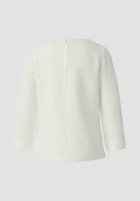 Weißes Oberteil mit strukturierter Oberfläche, 3/4-Ärmeln und einem Reißverschluss am Rücken. Schlichte, klare Linien mit rundem Ausschnitt.