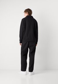 Black sweatshirt with a collar, paired with loose black trousers and white sneakers. Features ribbed cuffs and a relaxed fit.