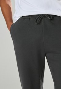 Grijze sweatpants van zachte stof, met een elastische tailleband met koord en zijzakken, getoond tegen een neutrale achtergrond.