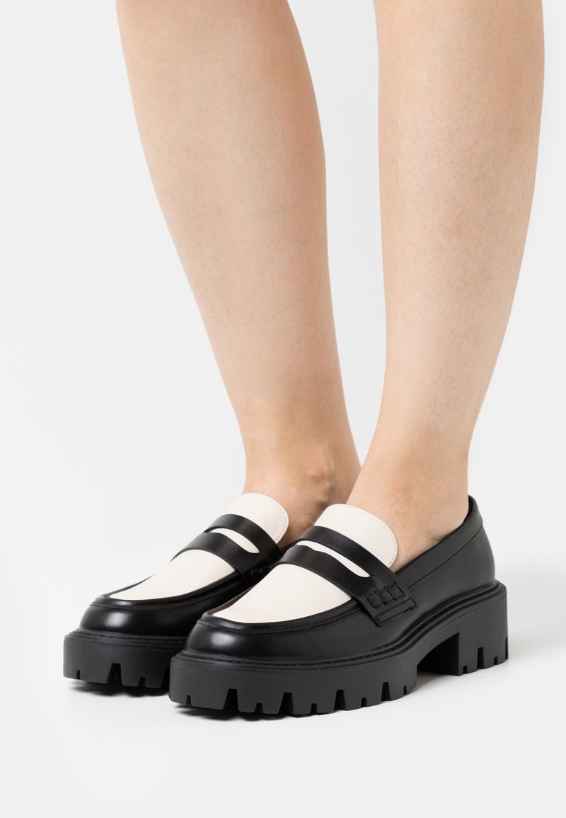 Mocassins à plateforme noir et blanc avec une surface en cuir lisse, deux sangles horizontales et une semelle épaisse texturée.