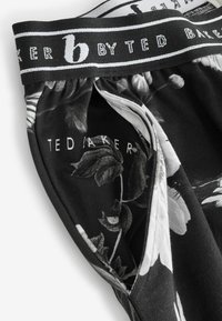 Čierne boxerky so vzorom kvetov a kontrastným bielym pásom s nápisom "BY TED BAKER" vytlačeným na čierno. Mäkka, ľahká látka.