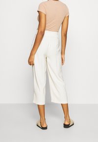 Haut beige clair côtelé à manches courtes associé à un pantalon large crème et des sandales noires à enfiler, vu de dos.