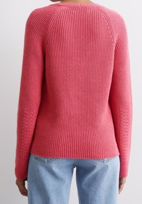 Pull en tricot rose avec une texture côtelée, des manches raglan et une coupe légèrement ample. Il présente de fines coutures le long des coutures latérales.