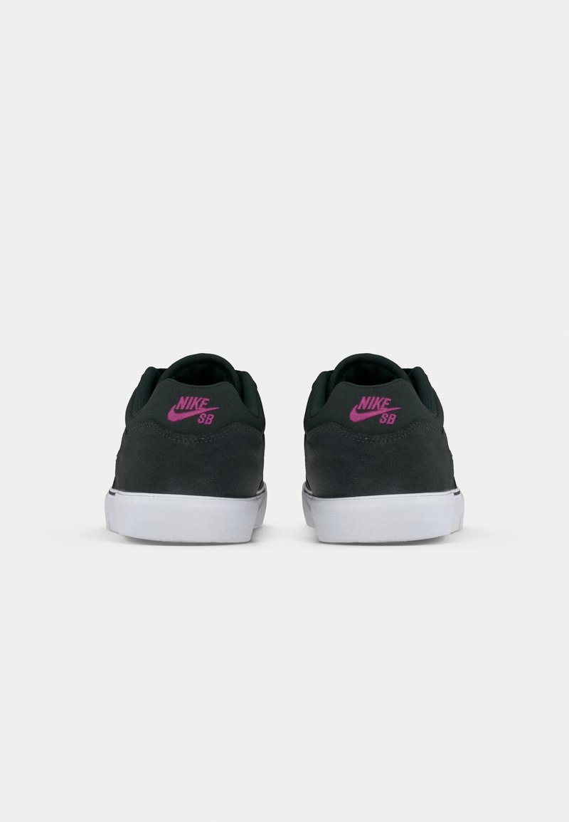Zapatillas Nike SB en ante gris oscuro con suelas de goma blanca y detalles en rosa en el talón. Forma redondeada, diseño minimalista.