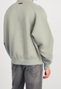 Ljusgrön fleece-tröja med hög krage, ribbade ärmslut och nederkant. Minimalistisk design med en liten logotyp på baksidan.