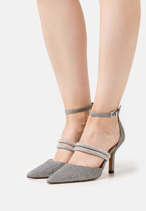 Chaussures à talons hauts en paillettes argentées avec bouts pointus et brides de cheville ornées de deux rangées de strass. Talons fins et texture lisse.