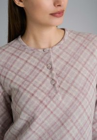 Maglietta a maniche lunghe rosa chiaro con un motivo a quadri di un rosa più scuro. Presenta un collo rotondo e tre bottoni di chiusura sul davanti. Tessuto morbido.