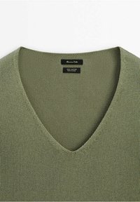 Pull en coton tricoté vert olive à col en V avec étiquettes de marque et d'entretien du tissu à l'intérieur de l'encolure.