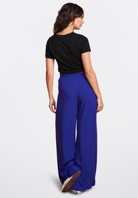 Top negro de manga corta combinado con pantalones de pierna ancha de cintura alta en un vibrante azul. Los pantalones cuentan con una textura suave y un diseño formal.