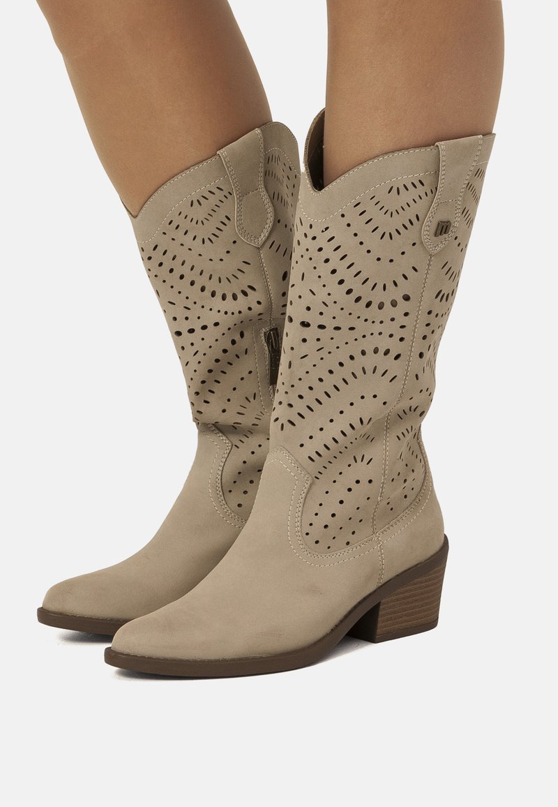 Botas de vaquero de ante beige con diseño perforado, punta afilada y tacón apilado de 2 pulgadas. Presentan una textura similar al denim y una abertura angular.