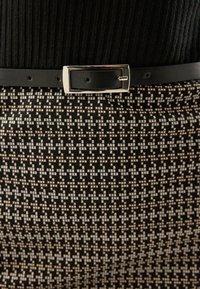 Melnas ribotas blūzes ar pieguļošu rakstainu svārku, kuram ir teksturēts bēšs un melns dizains, savilkti ar plānu melnu jostu ar sudraba sprādzi.