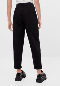 Black cotton trousers with a tapered fit, rolled cuffs, and a smooth texture. Features rear pockets and subtle stitching details.