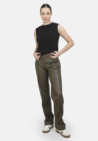Zwart mouwloos topje gecombineerd met olijfgroen neplederen broeken. De broeken hebben voornaadseams en een recht model. Casual witte sneakers.