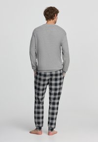 Maglietta grigia a maniche lunghe abbinata a pantaloni da pigiama a quadretti neri e grigi. Il design presenta una vita elastica e gambe affusolate.