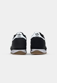 Zwarte sneakers met witte accenten en logo, textielstof, een gevoerde zool en een gumzool. Achteraanzicht toont logo op de hiel.