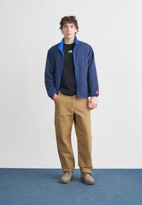 Ναυτικό μπουφάν με μπλε λεπτομέρειες, μαύρο μπλουζάκι, μπεζ παντελόνι και γκρι μπότες. Λείο ύφασμα, άνετη εφαρμογή και ελαστικά μανίκια. Απλός σχεδιασμός.