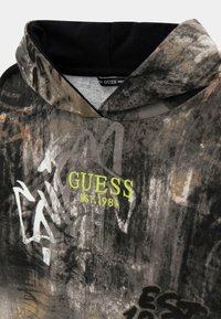 Felpa con cappuccio in grigio scuro con motivo astratto. Presenta il logo "GUESS EST.1981" ricamato in verde e cappuccio interno nero.