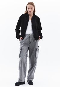 Felpa nera con zip e tasche frontali, abbinata a pantaloni cargo grigio chiaro con tasche laterali e una sottile texture a motivo. Calzature nere.