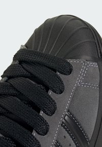 Μαύρο σουέντ αθλητικό παπο ύτσι με υφασμάτινη μαύρη λαστιχένια μύτη, μαύρα κορδόνια και αντίθετη λευκή ραφή κατά μήκος της πλευράς.