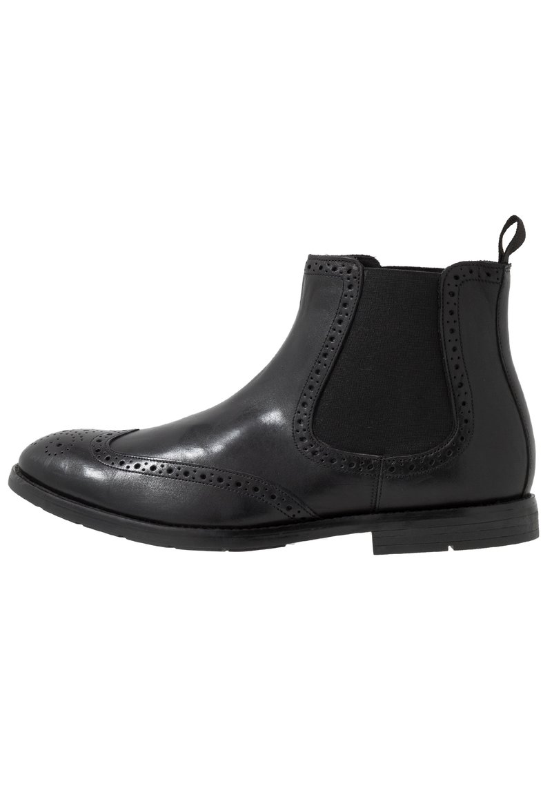 Zwarte leren Chelsea-boot met elastische zijpanelen, decoratieve brogue-details, ronde neus en een lage gestapelde hak. Gladde textuur overal.