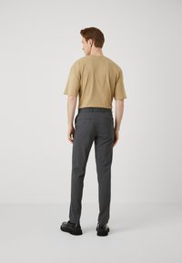 Beige short-sleeve t-shirt and dark grey tailored pants. Pants feature two back pockets; black shoes complete the outfit. Plain background.