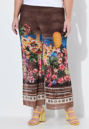Brązowe spodnie o szerokich nogawkach z kolorowym nadmorskim zachodem słońca, palmami, kwiatami i detalami z pismem, zestawione z żółtymi sandałami na słupku z paskami.